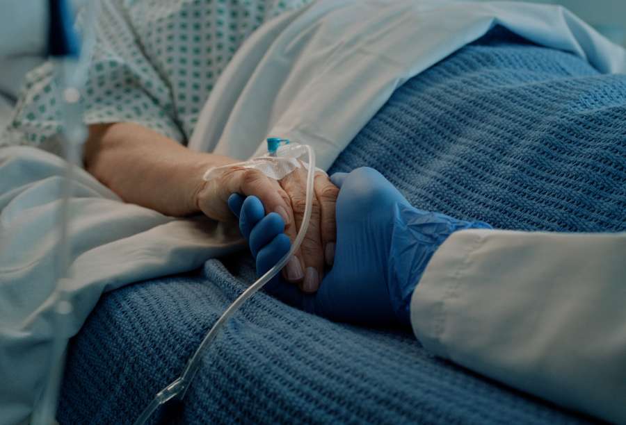 A patient lying in bed holding the hand of a healthcare professional
